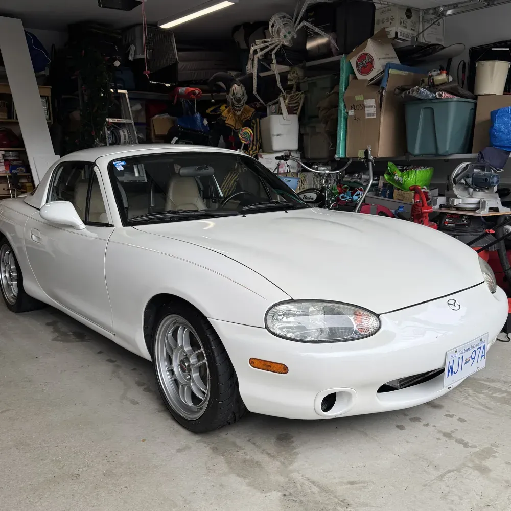 White Mazda Miata with a hardtop parked in the client's garage after an exterior detail