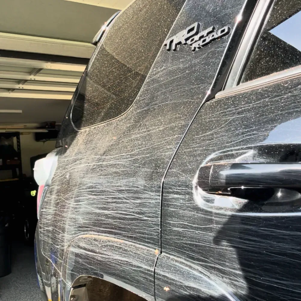 Heavy swirls and scratches on the rear quarter panel of a black Toyota 4Runner before paint correction
