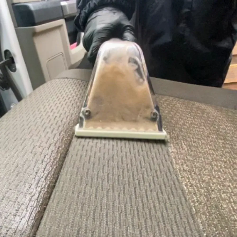 Extractor head pulling dirt out of a grey cloth seat, leaving a visibly cleaner stripe